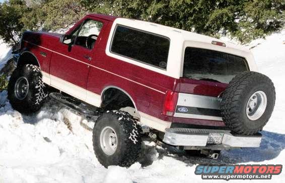Red and white Ford Bronco with large off-road tires and a spare tire on the back, driving in snow