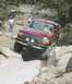 1993 Ford Bronco - A red Ford Bronco tackles a challenging off-road course with two people visible inside.