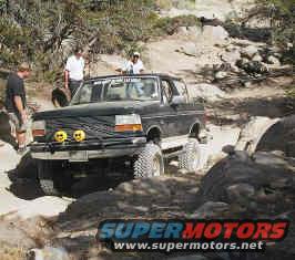 Black Ford Bronco navigating a rocky trail with two people inside and two standing nearby