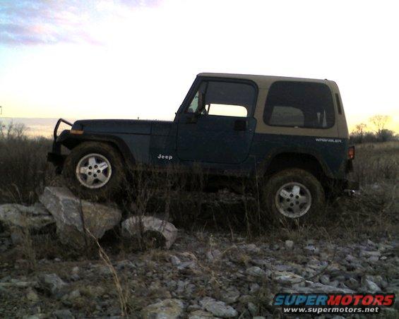 Dark green Jeep Wrangler with tan top on rocky terrain