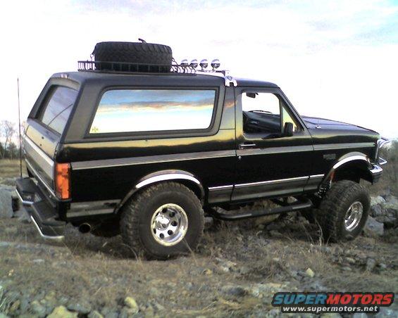 Black Ford Bronco with roof rack, spare tire, and aftermarket lights parked on rocky terrain