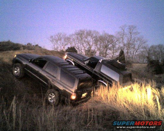 Two dark SUVs on a grassy incline at dusk, one behind the other