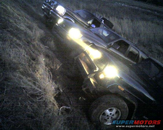 Two SUVs parked on a grassy slope at dusk, headlights on