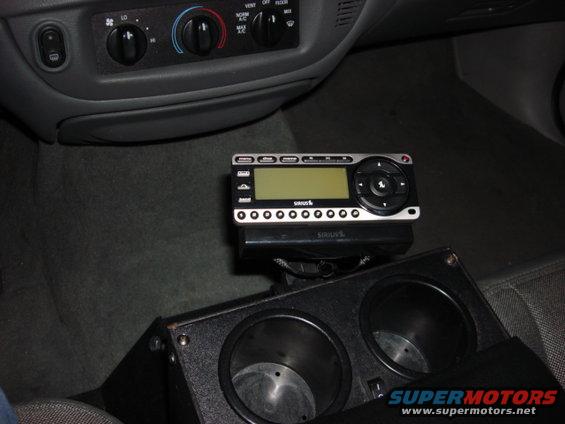 SiriusXM radio mounted above a double cup holder in a car's center console