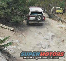 1993 Ford Bronco driving up a rocky dirt trail, another vehicle visible in background