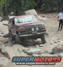 1993 Ford Bronco 3q-front view, red, off-roading on rocks with SuperMotors logo