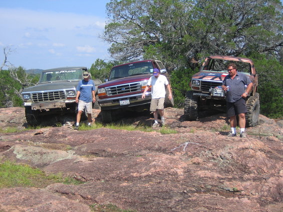 Three modified off-road trucks parked on rocky terrain
