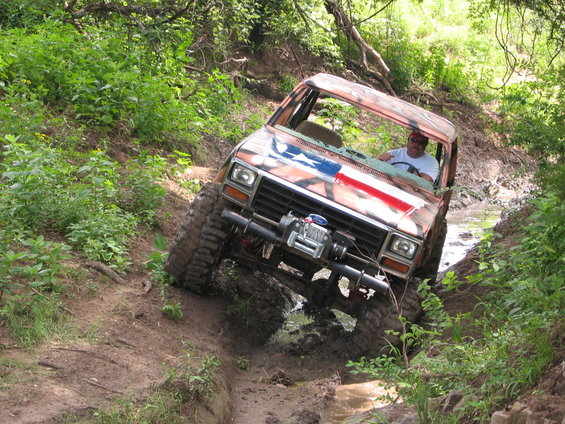 Modified Ford Bronco with American flag paint, off-roading through a muddy creek