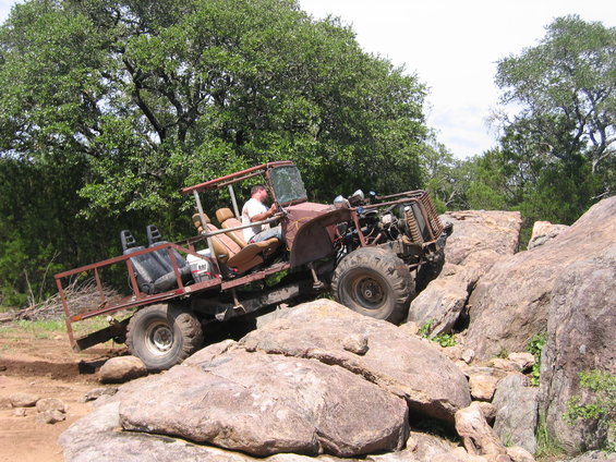 Custom off-road vehicle with exposed engine, roll cage, and flatbed, navigating large rocks