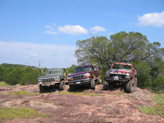 Three modified Ford Broncos parked on rocky terrain under a blue sky