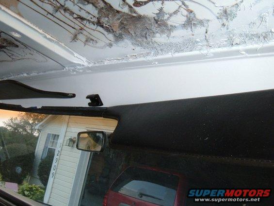 Interior view of a vehicle showing damaged headliner, side mirror, and a red SUV outside