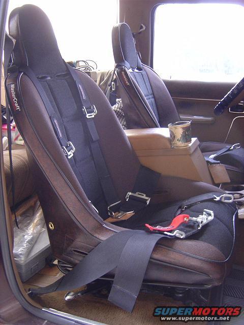 Interior view of a vehicle showing two bucket seats with racing harnesses and a center console