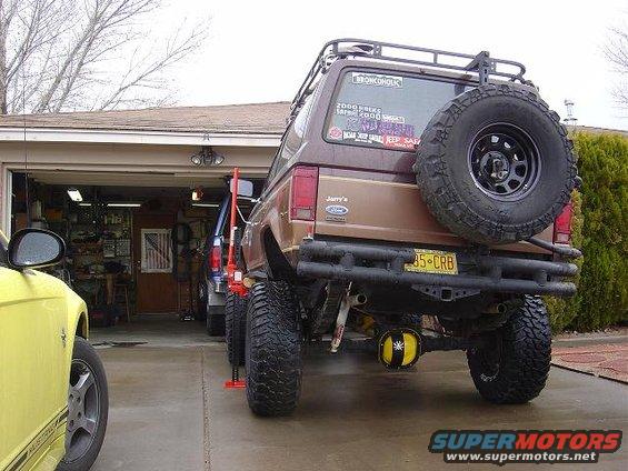 Brown Ford Bronco II with spare tire on back, parked in driveway near garage. Yellow Mustang in foreground