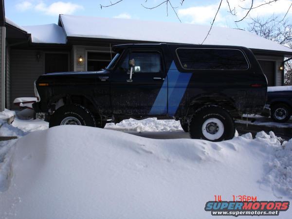 Side view of black 1979 Ford Bronco with blue stripe in snow