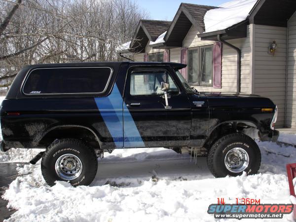 Black 1978 Ford Bronco with blue stripe parked in snow, side view. BFGoodrich tires visible