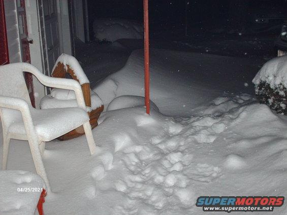 Plastic chairs and a planter covered in snow, with a red pole in the middle. Date stamp 04/25/2021