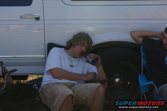 White van side view, man drinking from a bottle, another man in a chair