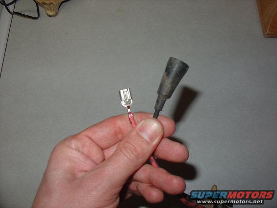 Hand holding a female spade connector and a black rubber boot for an electrical connector
