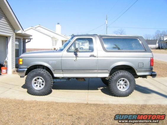 Side view of a lifted 1989 Ford Bronco with large tires parked in a driveway