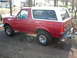 1995 Ford Bronco - This red Ford Bronco is shown from the rear quarter angle, parked on a dirt surface with houses in the background.