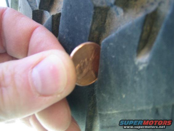 Penny measuring tread depth on a dark tire