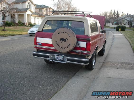 Red Ford Bronco parked on street, spare tire on back. Hood is up
