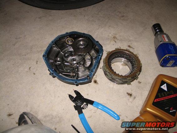 Disassembled motorcycle clutch assembly with tools and oil bottle on concrete floor