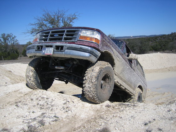 1996 Ford Bronco with lifted suspension and large tires navigating a dirt hill