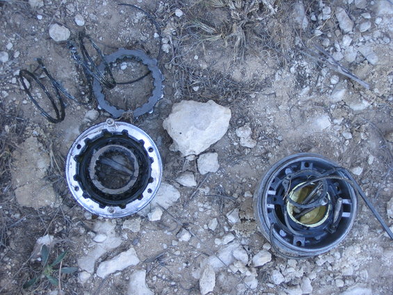 Disassembled vehicle parts, including gears and springs, scattered on rocky ground