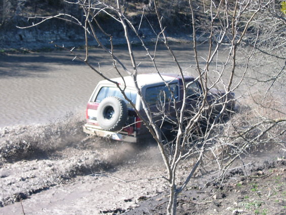 1996 Ford Bronco kicking up mud while driving off-road