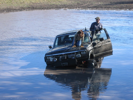 Black Ford Bronco stuck in shallow water with two people inside