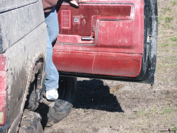Muddy interior door panel and wheel well of a vehicle with a person's legs visible stepping out