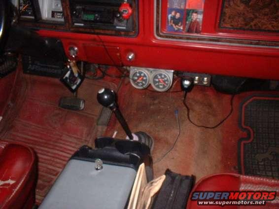 Vehicle interior with red seats, floor mats, and dashboard. Features a floor shifter, dual gauges, and a radio