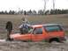 1984 Ford Bronco - An orange SUV is stuck in the mud with three people posing around it.