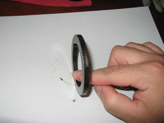 Metal ring held by a finger against a white surface with smudges