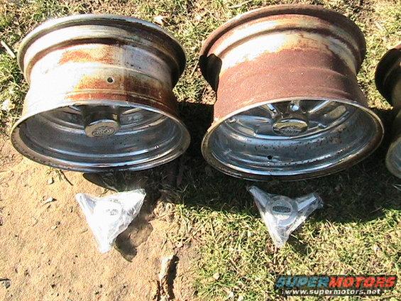Two rusty aluminum wheels with chrome centers and two hubcaps in plastic packaging on the ground
