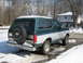 1994 Ford Bronco - This two-tone green and silver Ford Bronco is parked outside in a snowy environment, showing its rear profile and spare tire.