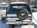 1994 Ford Bronco - The rear of a green Ford Bronco is shown with a spare tire cover and a snow-covered landscape.