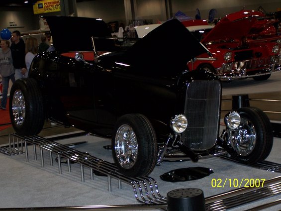 black hot rod convertible with hood open, chrome grille and wheels, on display