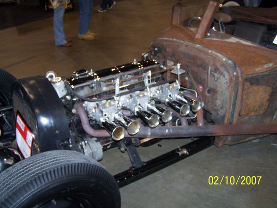 close-up of a V8 engine with multiple carburetors and chrome exhaust pipes on a rusty hot rod