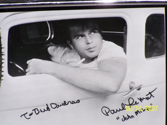 Black and white photo of a man leaning out of a car window, with signatures on the door