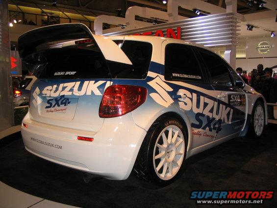 White Suzuki SX4 rally car with blue graphics and a large rear spoiler, viewed from the rear