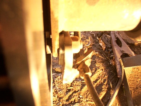 Close-up of a brake caliper and rotor assembly with a spring and metal bracket. Ground with debris is visible below