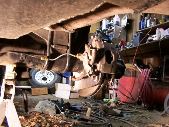 Rear axle and brake assembly on jack stands, with tools and equipment in background