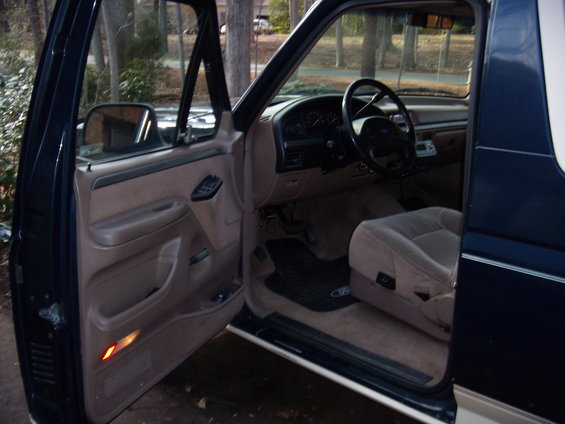 1992 Ford Bronco interior, driver's side door open, tan seats, dark dashboard, steering wheel visible