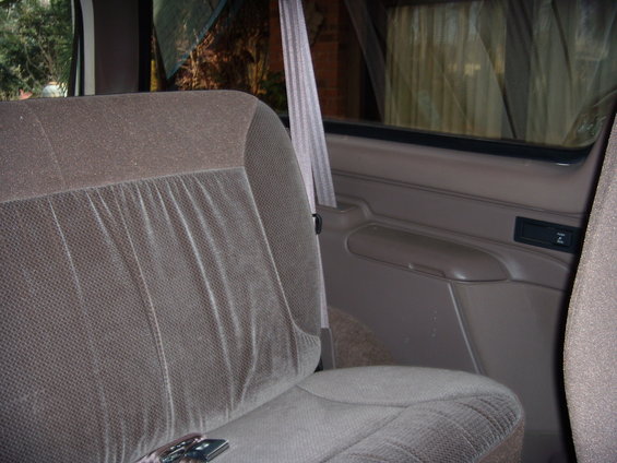 Back seat and door panel of a vehicle interior. Seatbelt visible