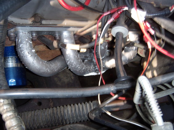Engine manifold with silver heat wrap and blue oil filter. Wires and hoses are visible