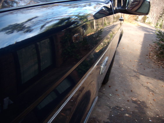 Side view of a 1992 Ford Bronco with chrome trim and a reflection of trees in the paint