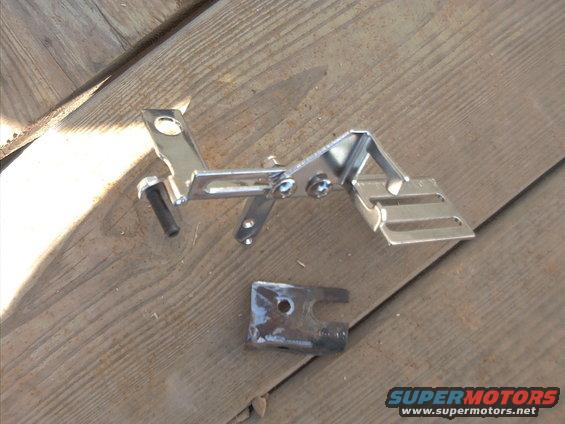 Metal bracket assembly with bolts on wooden planks. A smaller metal piece is nearby