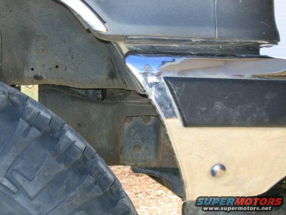 Chrome trim on black bumper section with large tire and suspension components visible